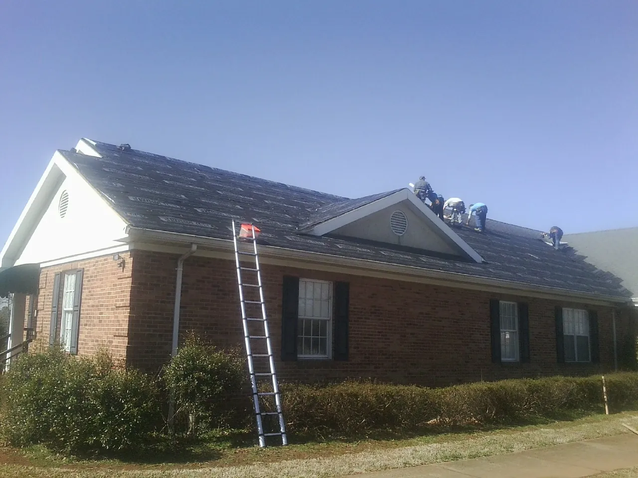 Crew tearing shingles off a brick ranch roof with a ladder set — Metal Roof Repair work by our crew in Grand Saline