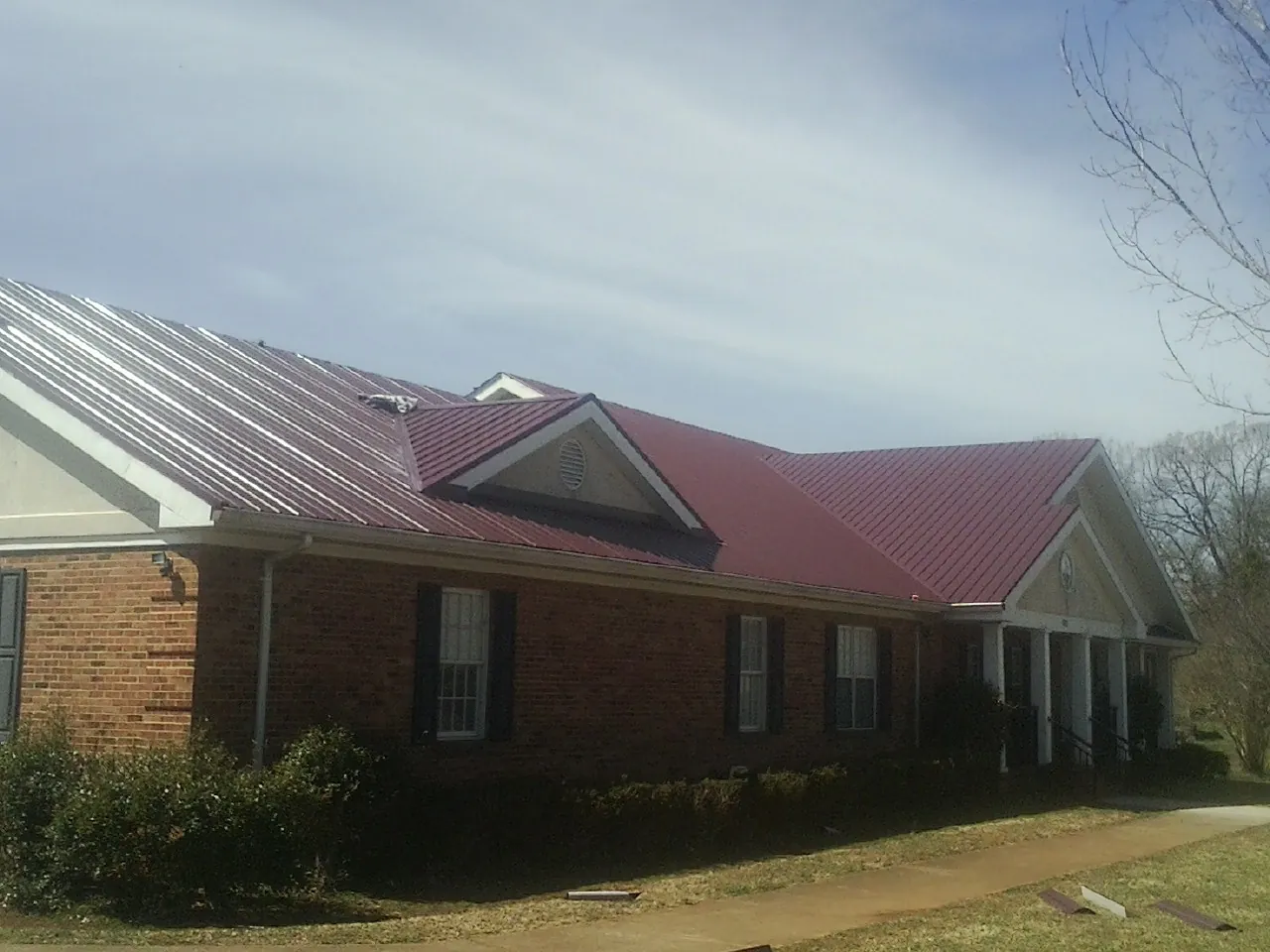 Red metal roof with gabled entries on a long brick building, from a Hail Damage Roof Repair job in Grand Saline
