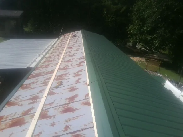 Old rusted panels beside newly installed green metal roofing — Wind Damage Roof Repair by Roofing Brothers in Grand Saline