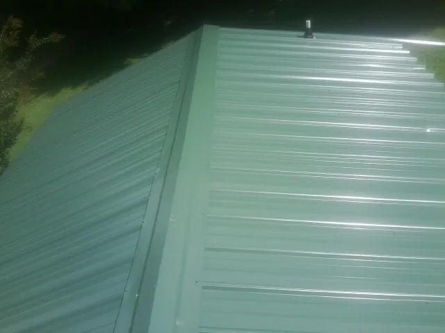 New green metal panels meeting at the ridge of a roof — Flat Roof Repair work by our crew in Grand Saline