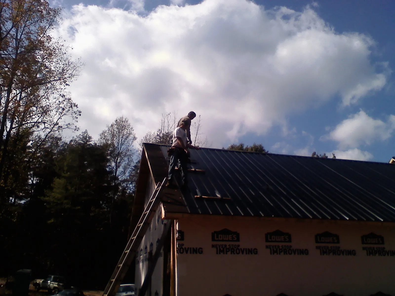 Roofer fastening dark metal panels high against a cloudy sky, from a Roof Inspection job in Grand Saline