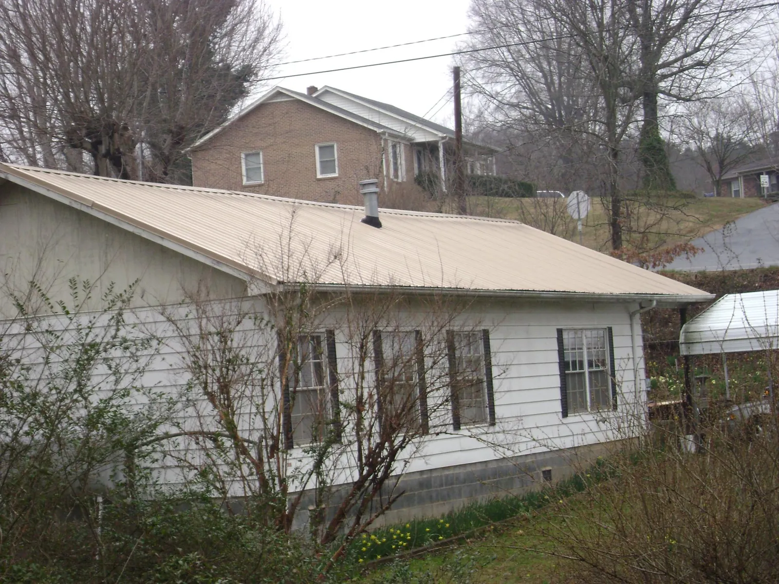 Tan metal roof on a white sided house set into a hillside — Commercial Roofing by Roofing Brothers in Grand Saline