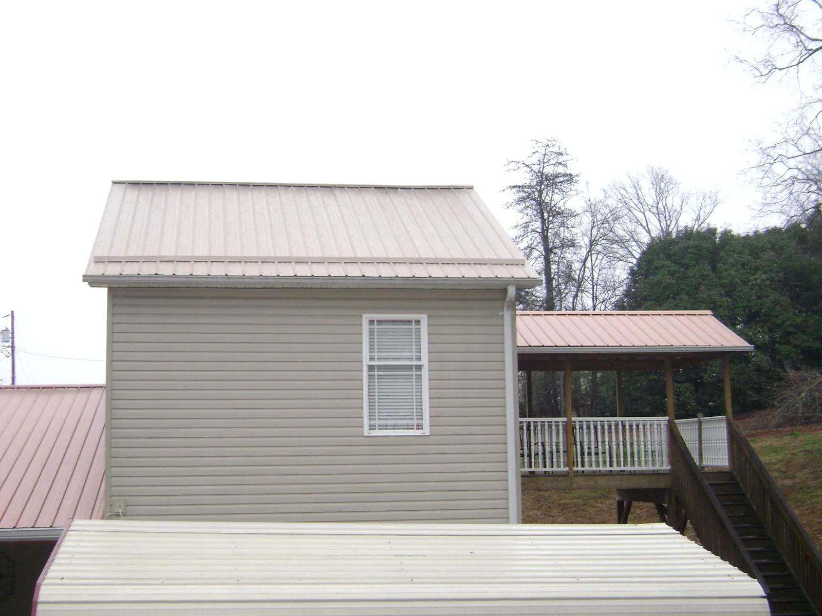 Tan metal roofs on a two story addition and attached porch, from a Roof Replacement job in Grand Saline